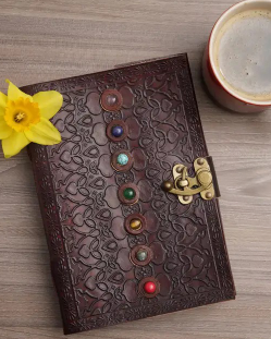 Leather-bound journal with chakra stones, daffodil, and coffee mug on wood table — perfect for tarot or spiritual journaling.