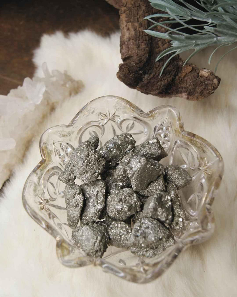 Raw pyrite crystal stones in a glass bowl on a fur surface with decorative crystals