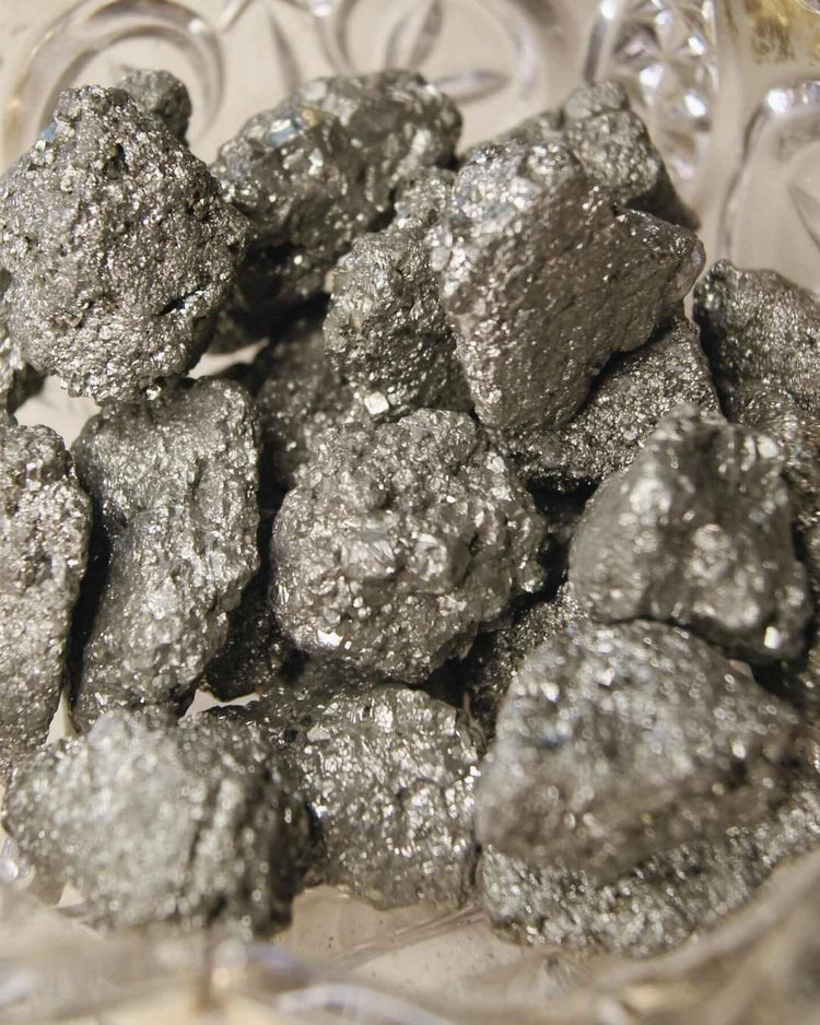 Rough pyrite crystal stones with metallic, shiny surfaces in a decorative glass bowl.
