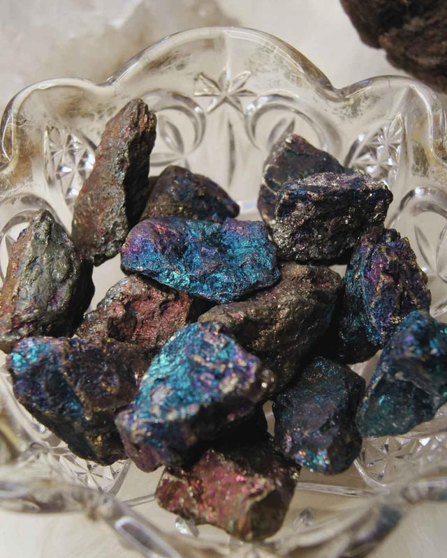 Iridescent raw peacock ore healing crystals in a clear decorative bowl