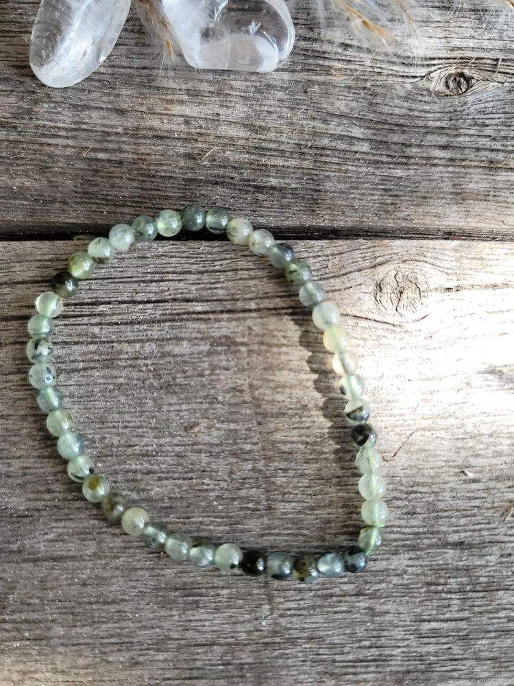 Prehnite crystal bead bracelet on rustic wood with clear quartz crystals nearby