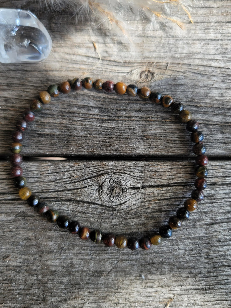Tiger’s eye beaded bracelet on rustic wood with crystal and feather accents