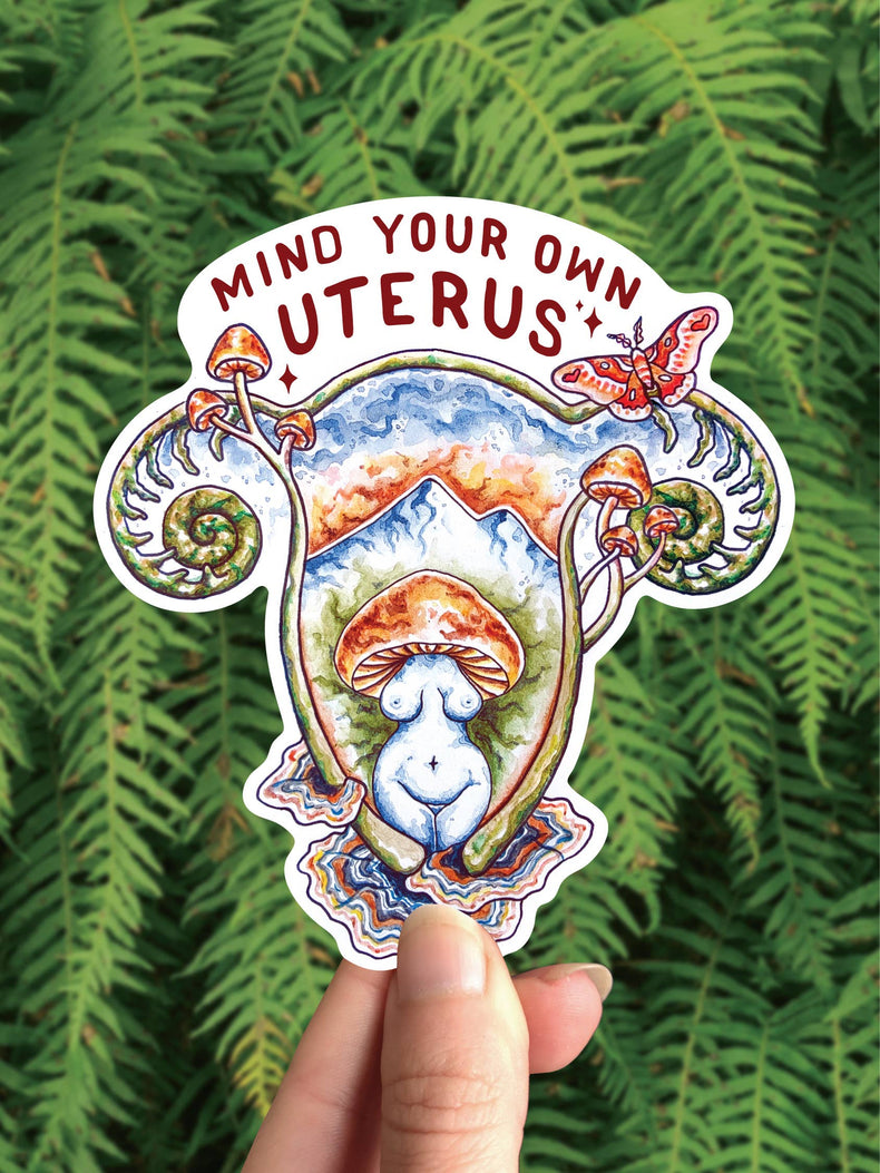 Mind Your Own Uterus vinyl sticker, a uterus shaped landscape with mushrooms and a goddess figure