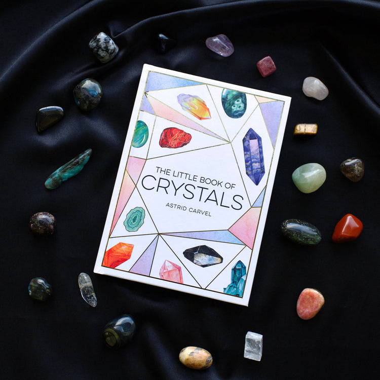 The Little Book of Crystals on black fabric, surrounded by assorted healing crystals