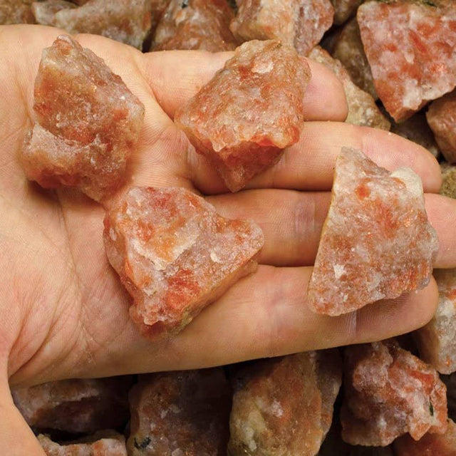 Hand holding rough orange crystals, healing stones, natural mineral rocks