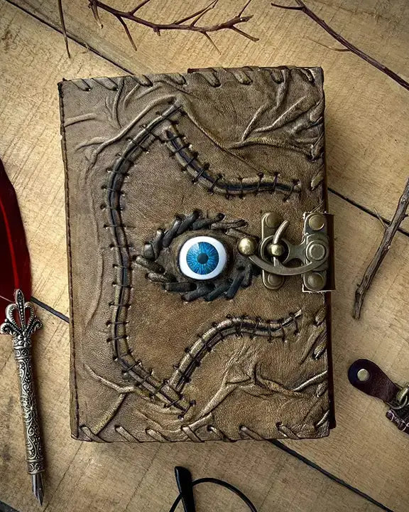 Mystical leather-bound journal with blue eye, stitching, and metal clasp, surrounded by feathers and branches