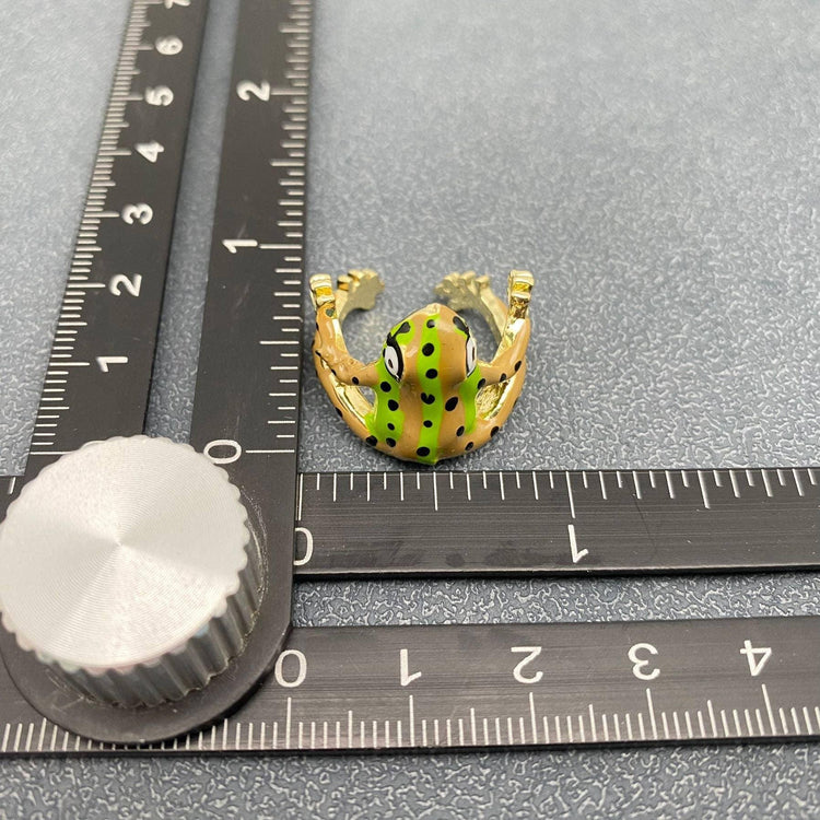 Green and yellow frog ring with black spots measured against a ruler on gray background
