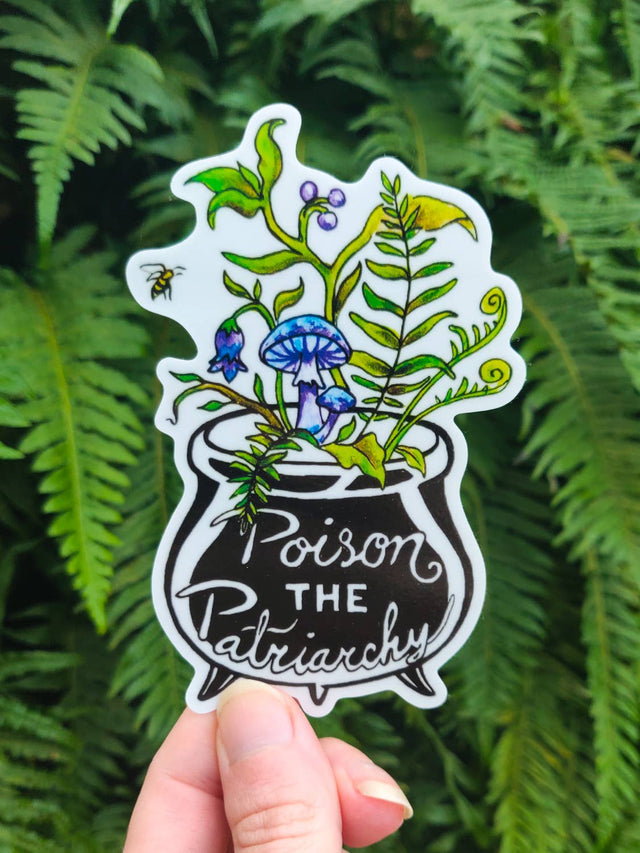 Poison the Patriarchy vinyl sticker, a black cauldron full of ferns, belladonna and mushrooms, held against green ferns
