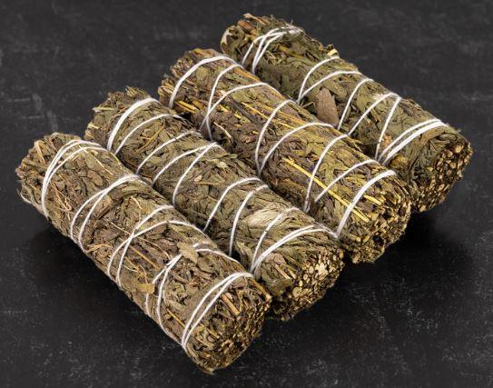 Four dried sage bundles wrapped with white string on a dark surface for cleansing rituals