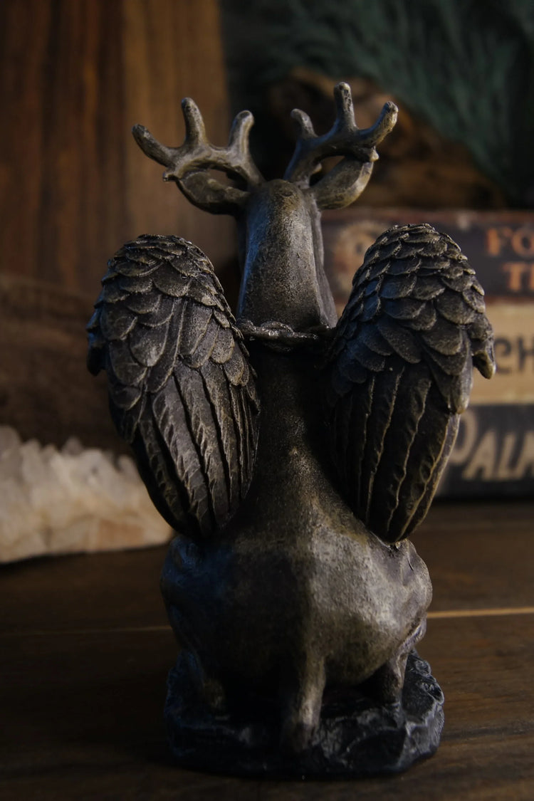 Antlered winged animal statue on wooden table with crystals and mystical decor