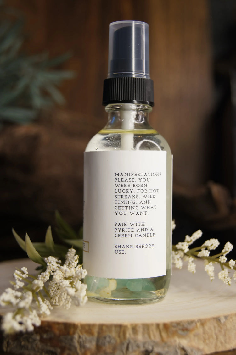 Clear spray bottle with manifestation ritual label, crystals inside, and white flowers on wood slice.