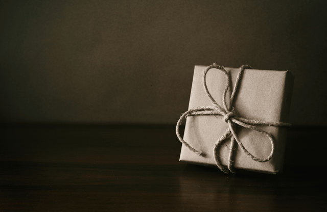 A small brown kraft paper gift box tied with twine on a dark wooden surface.