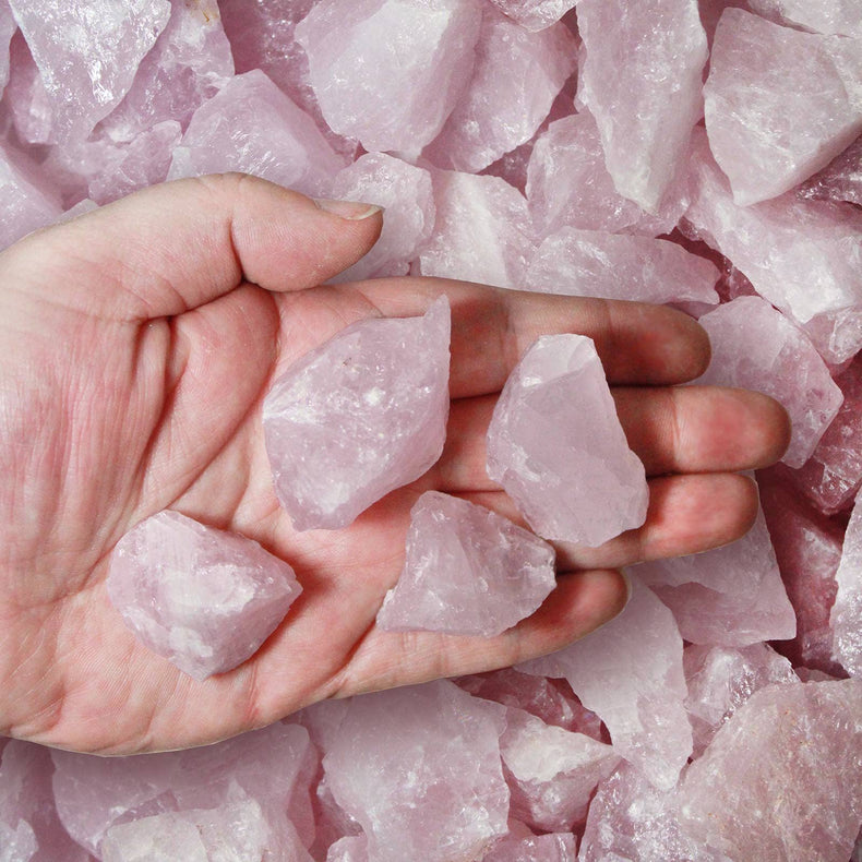 Hand holding raw rose quartz crystals, surrounded by pink healing stones