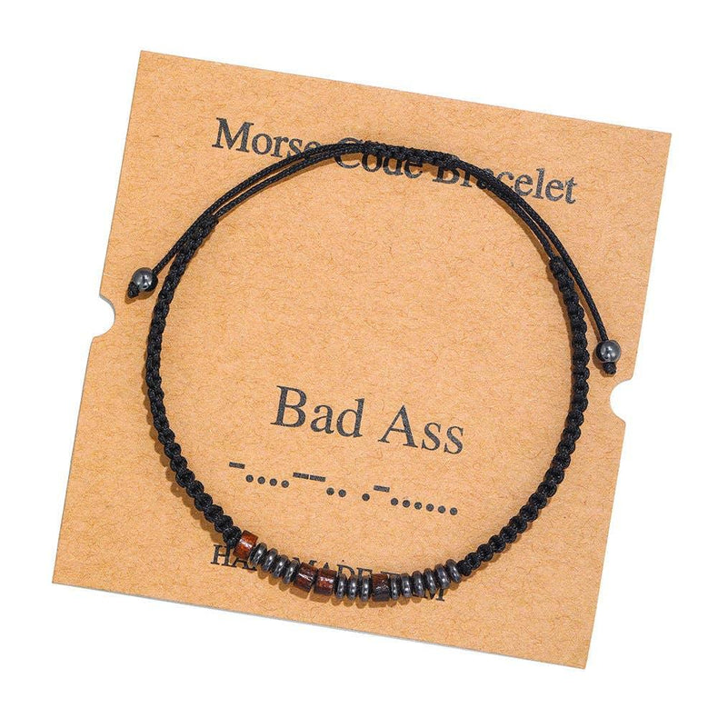 Black cord morse code bracelet with metallic beads on kraft card labeled 'Bad Ass'.