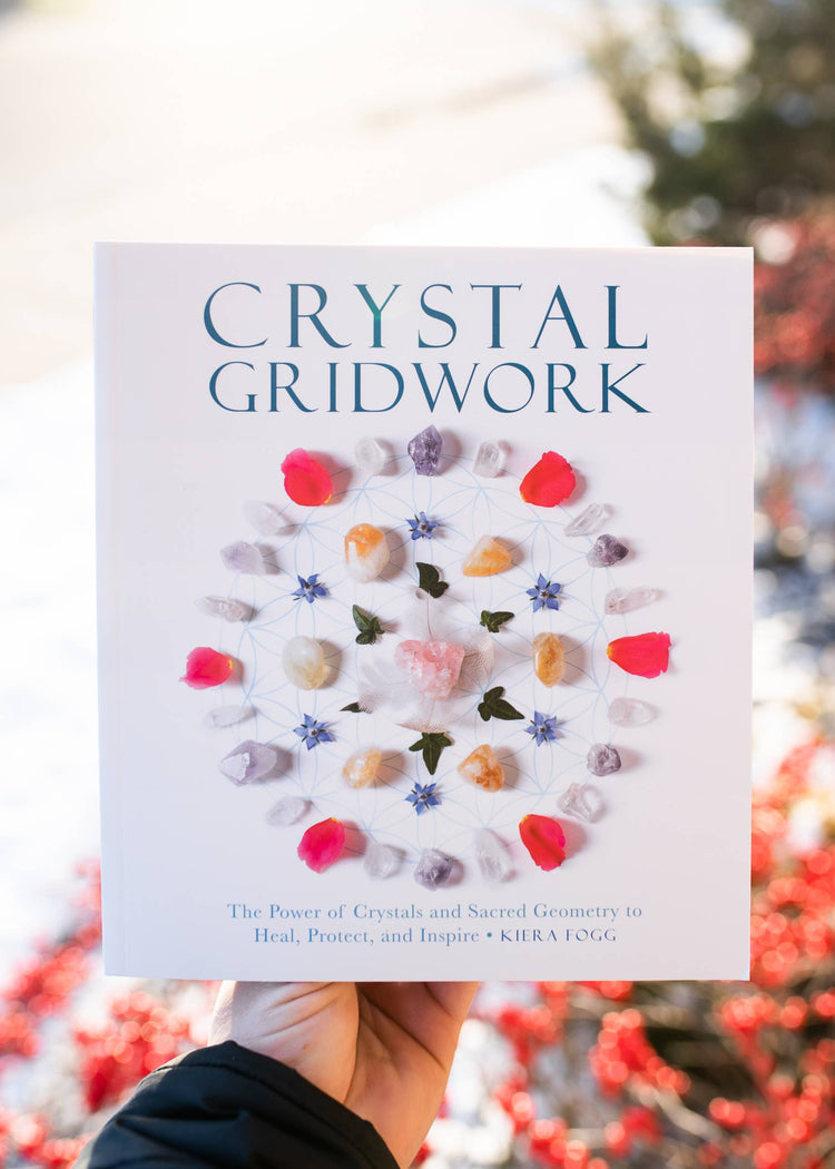Hand holding 'Crystal Gridwork' book with colorful crystal grid design on the cover