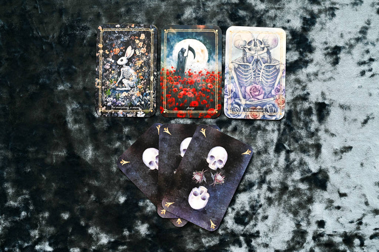 Tarot card set with illustrated skeletons, skulls, and flowers on a velvet background