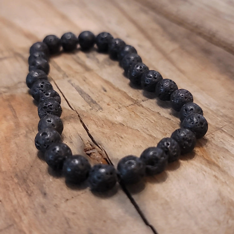 Black lava stone beaded bracelet on rustic wooden surface, metaphysical jewelry