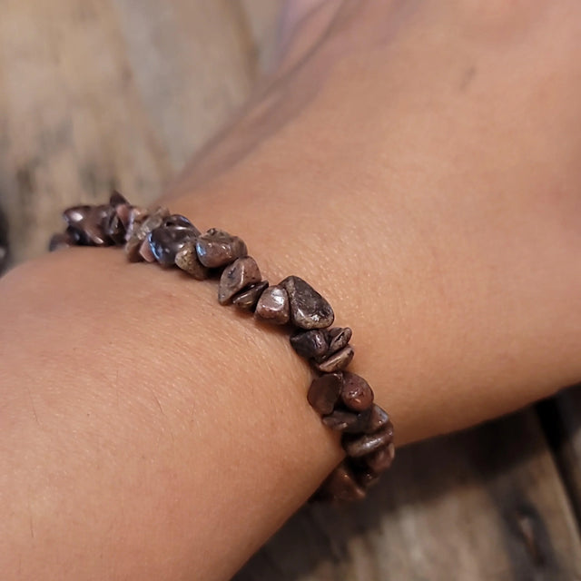 Rhodonite chip stone bracelet on wrist, natural crystal jewelry on wooden background