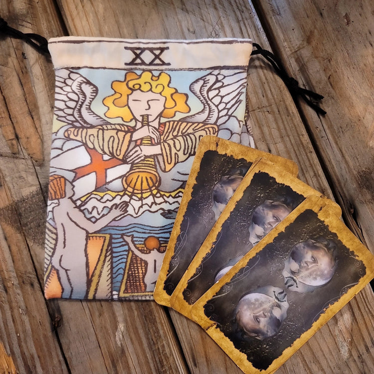 Tarot card pouch with angel design and three tarot cards on rustic wood table
