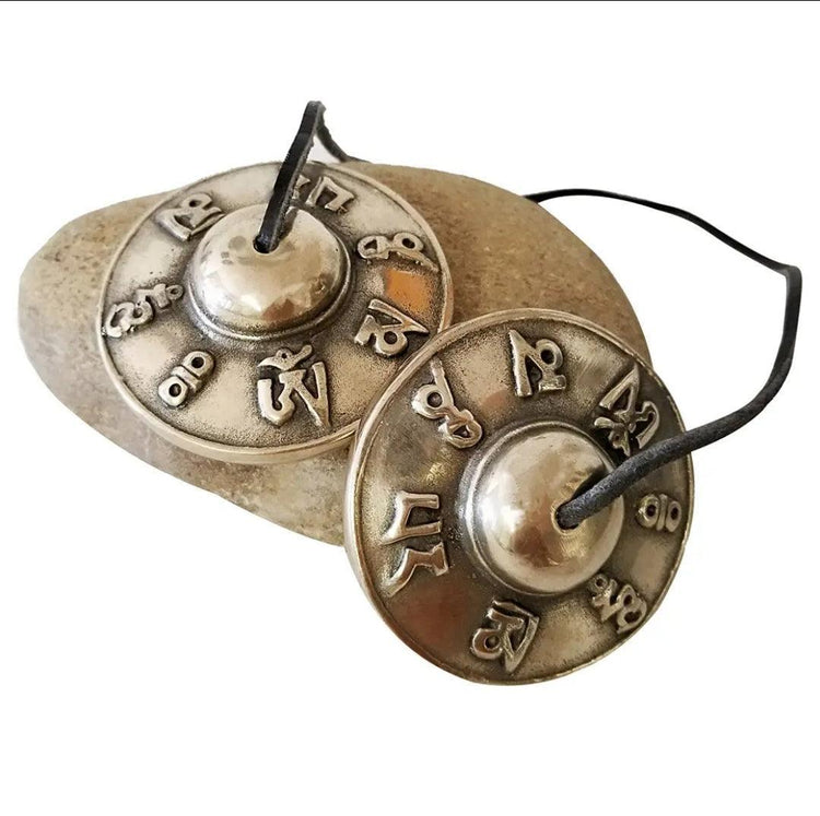 Pair of Tibetan tingsha cymbals with embossed Sanskrit symbols on a stone