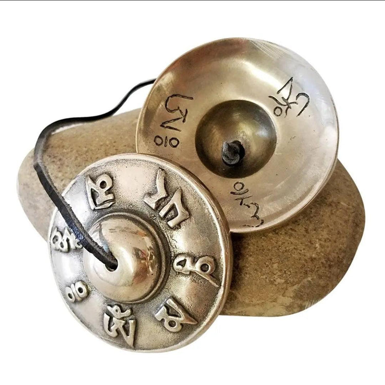 Brass Tibetan tingsha chimes with embossed Sanskrit symbols on a stone, meditation tool.