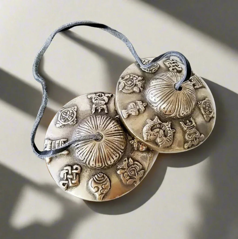 Tibetan tingsha chimes with engraved symbols on a cord, used for meditation and rituals