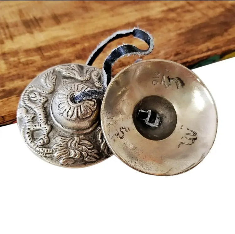 Tibetan tingsha chimes with engraved patterns and a black leather cord on wood table