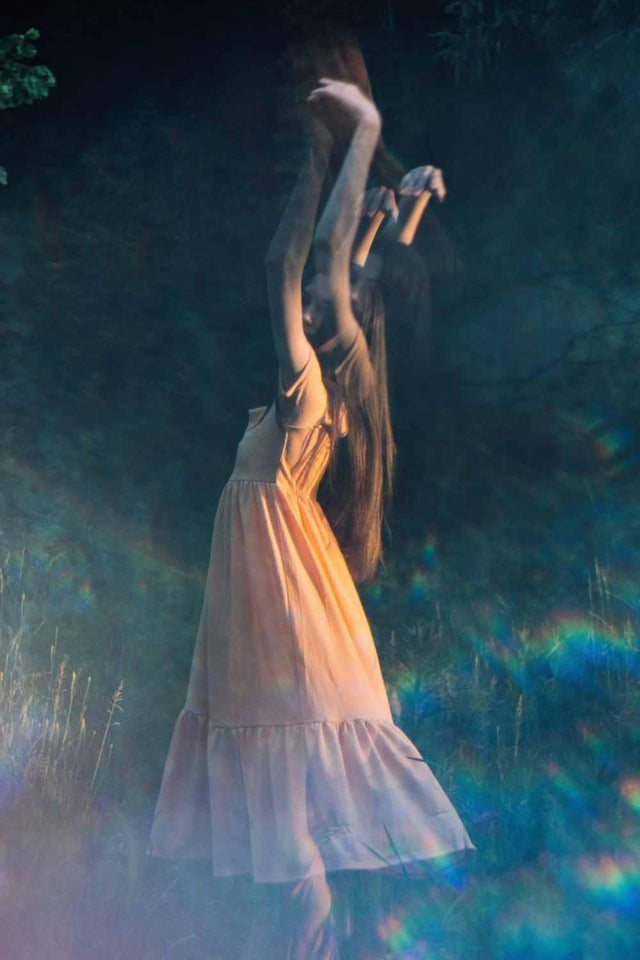 Woman in a flowing dress dancing in mystical forest light with ethereal motion blur
