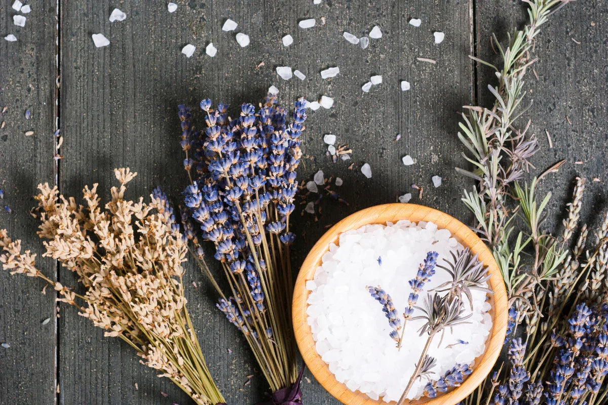 Herbal bundles, dried lavender, and a wooden bowl of bath salt on rustic wood background