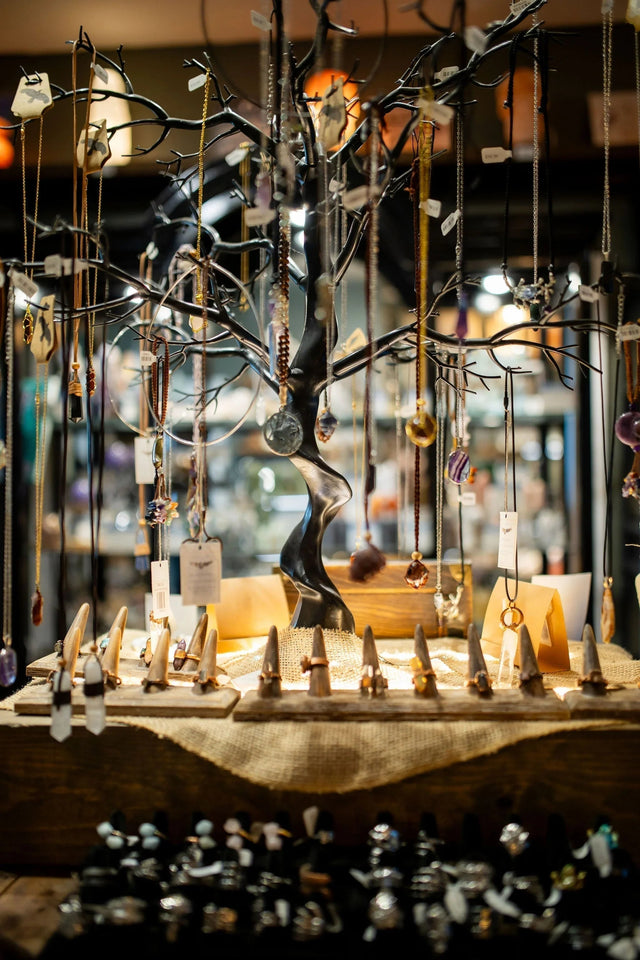 Crystal pendant necklaces and gemstone rings displayed on a metal jewelry tree in a metaphysical shop