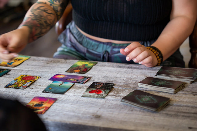 Person doing tarot card reading on rustic table with colorful tarot cards spread out