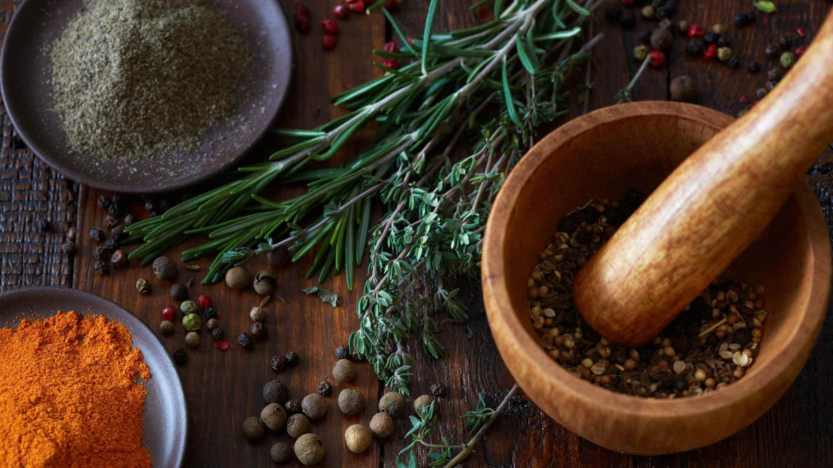 Herbs, spices, and peppercorns with a wooden mortar and pestle on rustic table