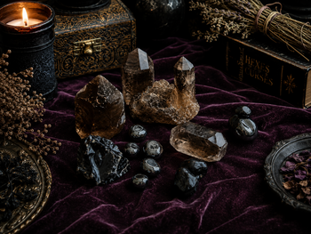 Black candles and assorted healing crystals on a dark wooden table with rosemary sprigs
