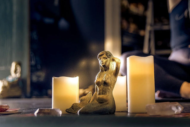 Mermaid figurine surrounded by glowing candles and crystals in a mystical setting
