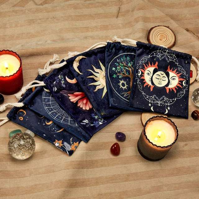 Tarot card bags with celestial designs, candles, and crystals on fabric background