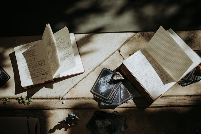 Tarot cards, crystals, and open notebooks with handwritten notes on a sunlit stone surface