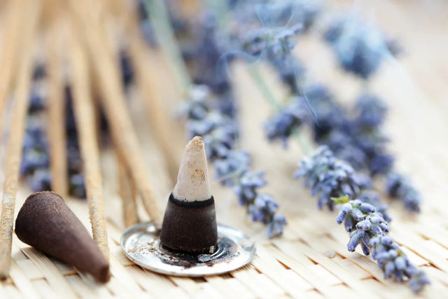 Incense cones, sticks, and lavender flowers arranged on a woven mat for aromatherapy or meditation.