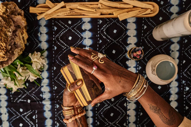 Hands shuffling tarot cards with crystals, incense, and ritual items on a patterned cloth.