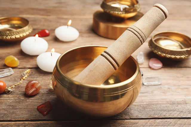 Brass singing bowl with wooden mallet, crystals, gemstones, and candles on wooden table