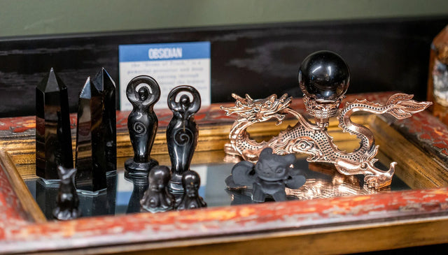 Obsidian crystal points, goddess figurines, and a dragon stand with a black sphere on a tray