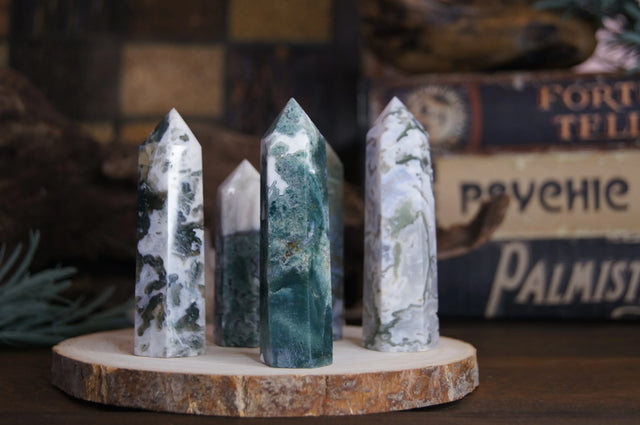 Polished moss agate crystal towers on wood slice with psychic decor background