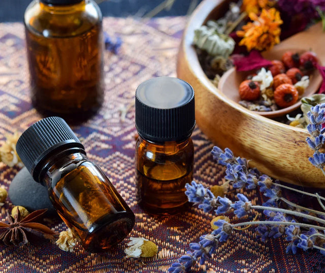 Essential oil bottles with dried lavender and herbs on a patterned cloth, holistic wellness