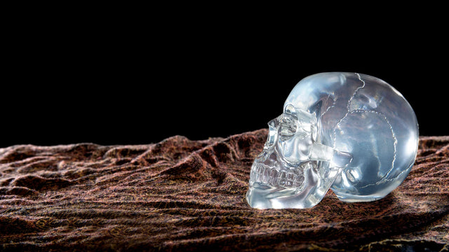 Clear crystal skull on textured brown cloth with black background, metaphysical decor