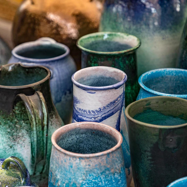 Handmade ceramic cups and pitchers in blue and green glaze on display