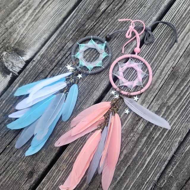 Two dreamcatchers with pastel feathers and star charms on weathered wood background