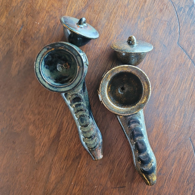 Two handcrafted ceramic pipes with removable lids on a wood surface, rustic style