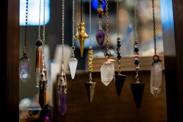 Assorted crystal pendulums on chains displayed in a metaphysical shop setting.