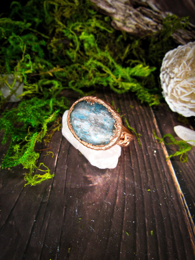 Copper wire-wrapped gemstone ring displayed on crystal with mossy, rustic background