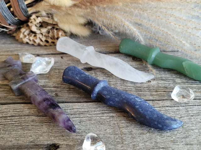Crystal ritual knives in various colors on rustic wood with dried herbs and decorative stones