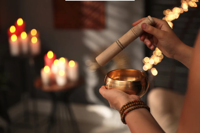 Person using a Tibetan singing bowl in a calming room with candles and soft lights.